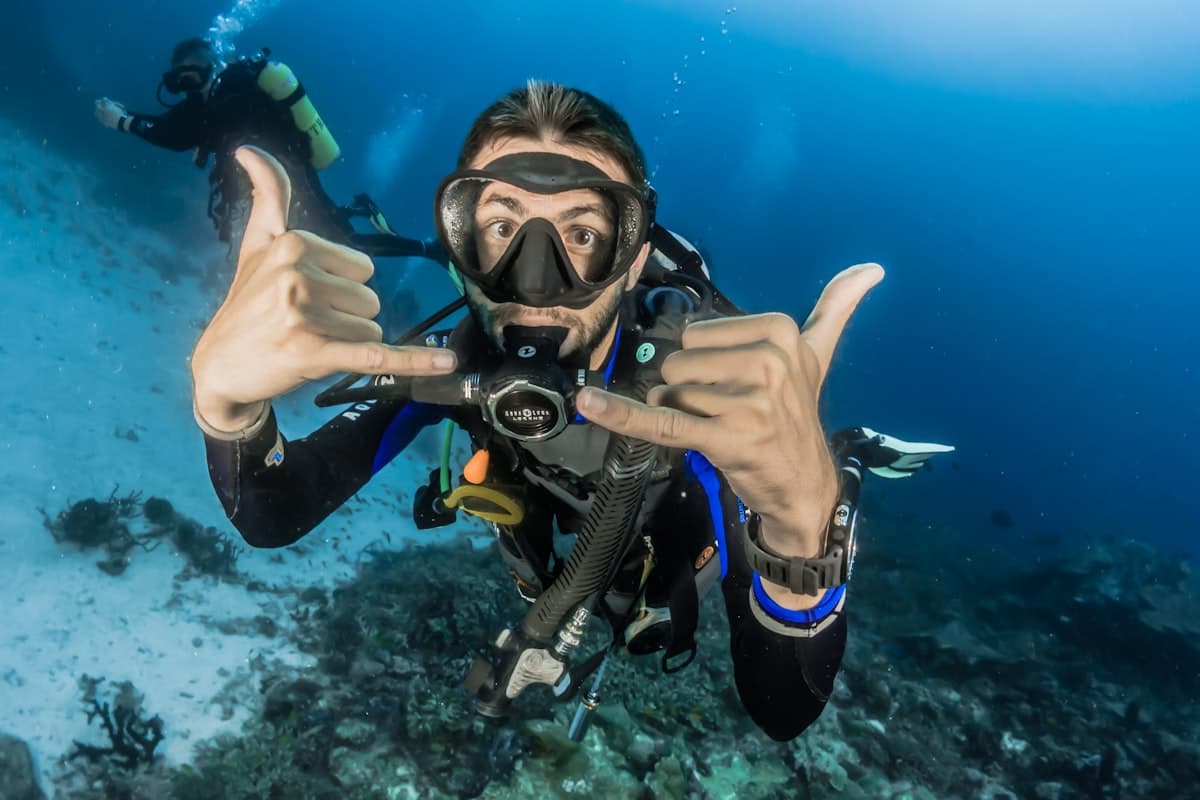 A scuba instructor underwater making an OK hand signal to a first-time diver